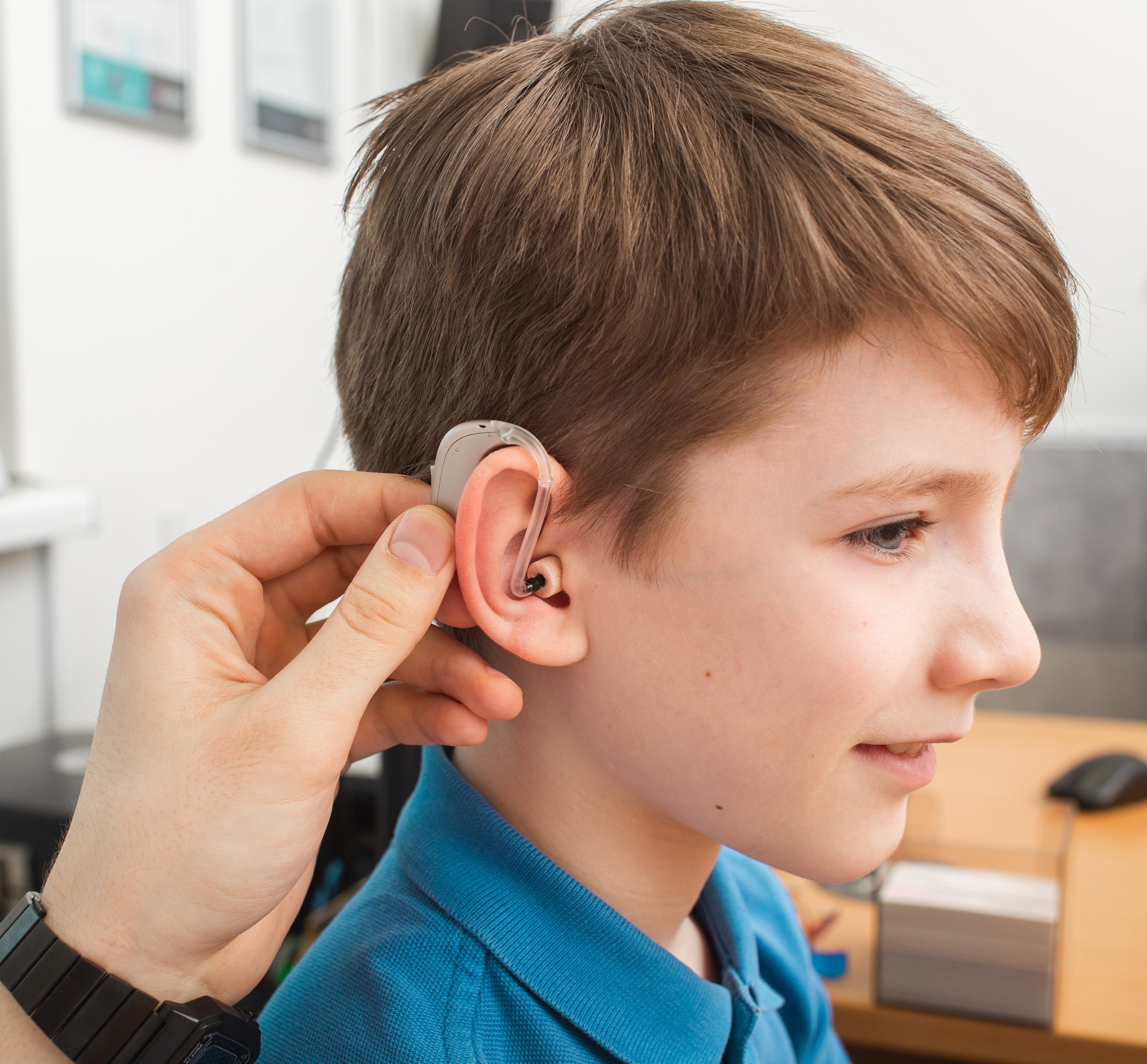 Installation hearing aid on сaucasian boy's ear. Hearing treatment at clinic