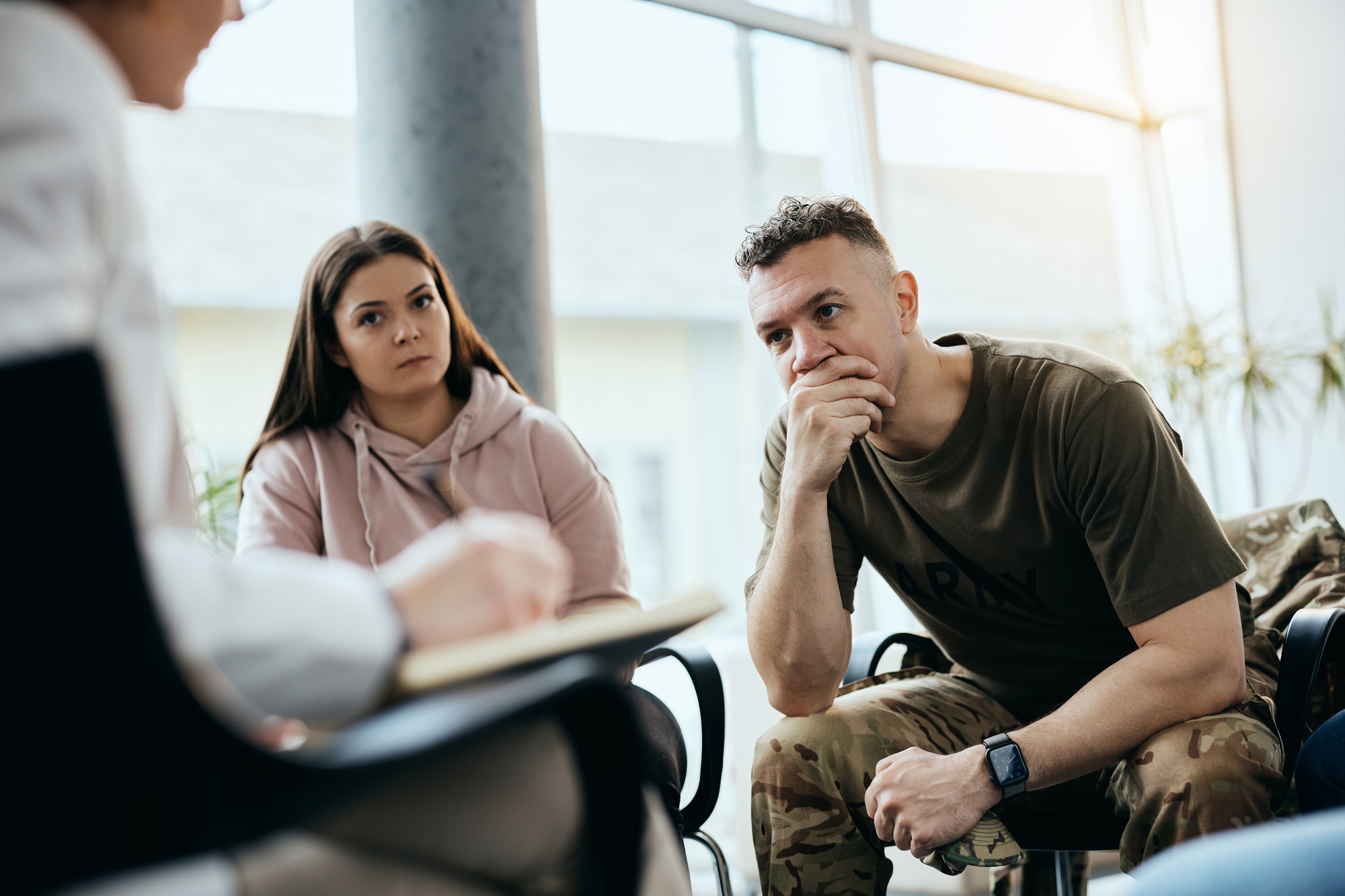 Stressed military man listening group therapist during counseling at mental health center.