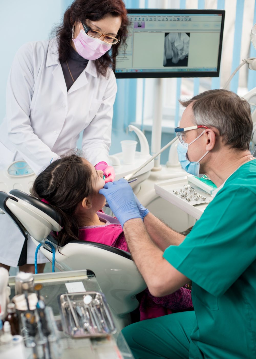 Girl with on the first dental visit. Senior pediatric dentist with nurse treating patient teeth